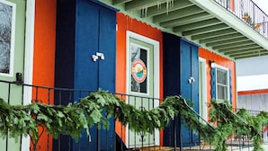 Un edificio colorido con un balcón, una puerta con un logotipo y una barandilla con plantas.