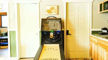 Uma mesa de shuffleboard numa sala com soalho de madeira e um tapete estampado.