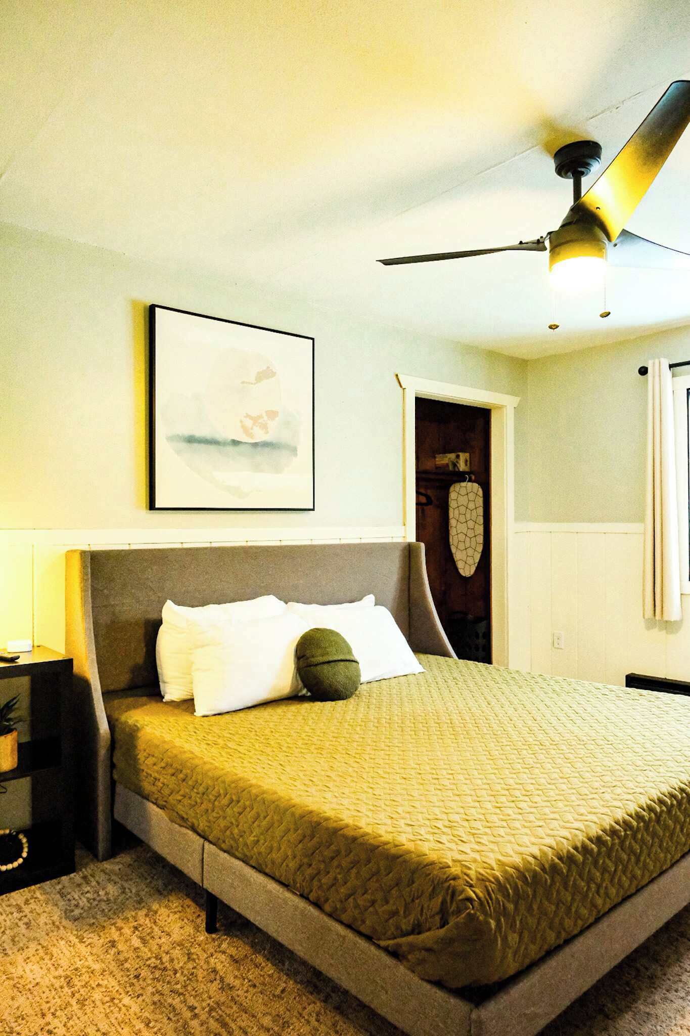 A bedroom with a bed, a ceiling fan, a framed picture on the wall, and a door leading to a closet.