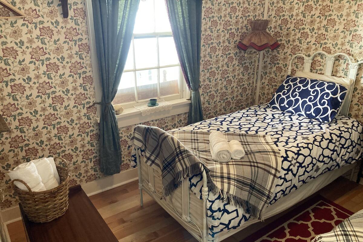 Une chambre à coucher avec un lit, une fenêtre avec des rideaux, une table de chevet et un mur décoré de motifs.