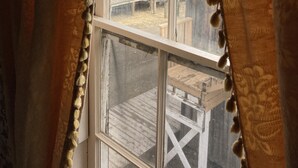 A window with a view of a building and a forest. - St. George Hotel (Barkerville)