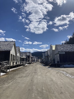 A historic town street with buildings, a dirt road, and a mountainous backdrop. - St. George Hotel (Barkerville)