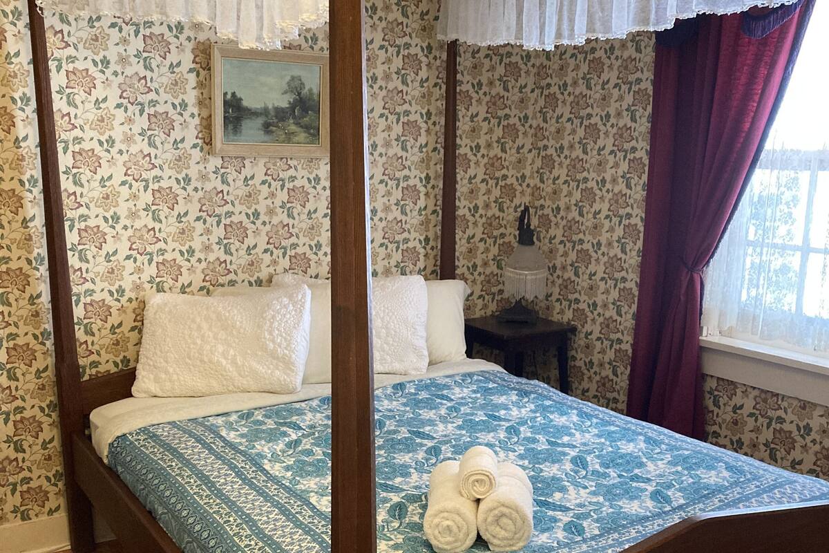 Un lit à baldaquin avec une couvre-lit à motifs bleus et blancs, une tête de lit en bois et un tapis à motifs rouges et blancs.