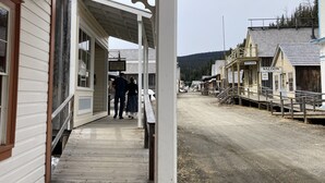 A wooden building with a porch, a sign for a restaurant, and a sign for a coffee shop. - St. George Hotel (Barkerville)