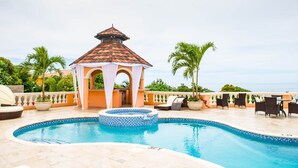 A swimming pool with a hot tub, lounge chairs, and a gazebo.