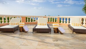 A rooftop terrace with four wicker lounge chairs, each with a white cushion and a yellow and white striped pillow.