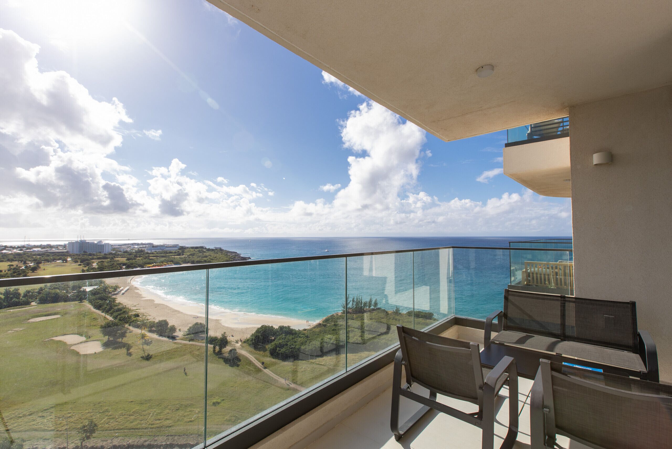 A balcony with a glass railing overlooking a beach and ocean.