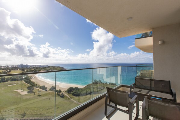 A balcony with a glass railing overlooking a beach and ocean.