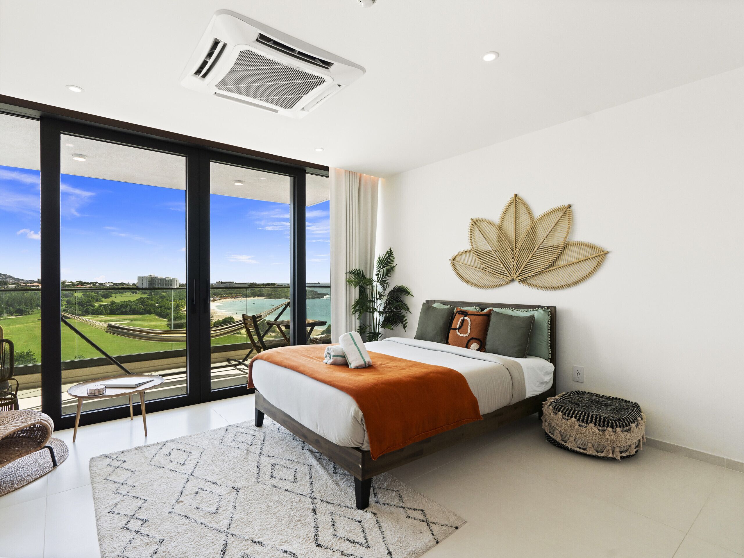 A modern bedroom with a large bed, a view of a beach and golf course, and a ceiling fan.