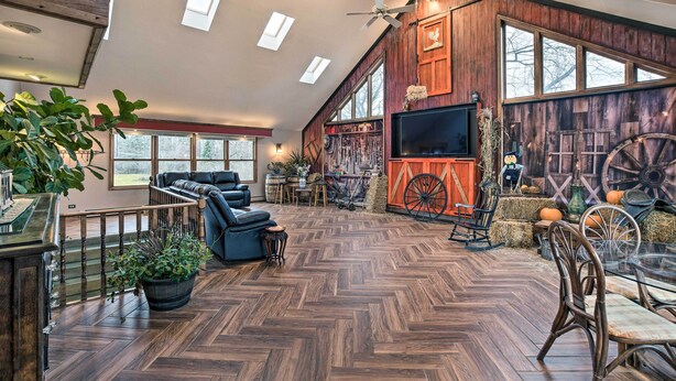 Uma sala de estar ampla com piso em padrão herringbone, uma TV grande e decoração rústica, incluindo uma roda de carroça e fardos de feno.