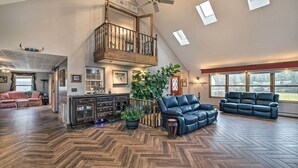 Uma sala de estar ampla com piso de madeira em padrão herringbone, um sofá de couro preto, uma mesa de centro de madeira e uma grande planta em vaso.