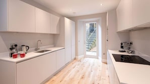 Une cuisine moderne avec des meubles blancs, un plancher en bois et une vue sur un escalier menant à l’extérieur.