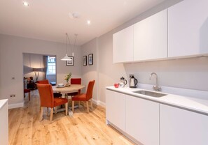 A modern kitchen with white cabinets, a stainless steel sink, and a dining area with a wooden table and orange chairs. - Elegant 2-bedroom apartment in Edinburgh’s West End for families, corporate stays and digital nomads (Edinburgh)