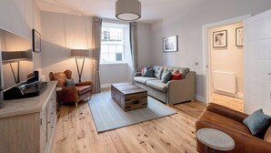 Un salon moderne comprenant un canapé, un fauteuil, une table basse en bois et un téléviseur.