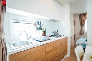 Una cocina compacta con un lavamanos, armarios de madera, una estufa y utensilios colgantes.