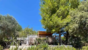 A house with a wooden deck, surrounded by dense greenery and trees. - Mobilehome with air conditioning, terrace and pool (Peschici)