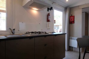 Una cocina moderna con estufa a gas, horno integrado, pileta y ventana con cortinas. Hay un extintor de incendios colgado en la pared y un termostato a la derecha.