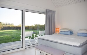 Een slaapkamer met een grote schuifdeur naar een tuin, een bed met kussens, een nachtkastje met een lamp en een bankje.