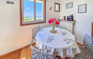 Un comedor con una mesa lista para dos personas, una ventana con vista al mar y un radiador sobre la mesa.