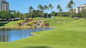 Un campo da golf con uno stagno, palme e un edificio sullo sfondo.