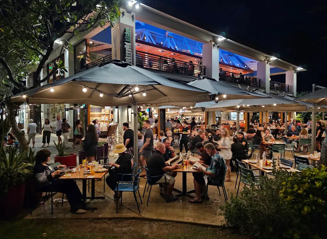 Un espacio exterior para comer con varias mesas y sombrillas, rodeado por un edificio con un letrero de restaurante visible.
