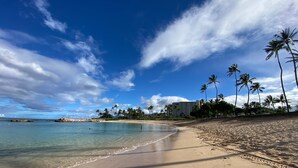 Una spiaggia con acqua cristallina, palme e un edificio sullo sfondo.