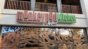 Segnaletica di un ristorante con un design raffigurante una scimmia e il nome 'Monkeypod Kitchen'.