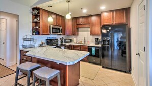 A modern kitchen with a marble island, stainless steel appliances, wooden cabinets, and pendant lighting. - 3rd-Floor Riverfront Condo: Walk to Downtown Eats! (Darien)