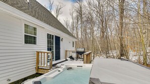 Ein Whirlpool in einem Hinterhof mit einem Haus, einer Holzterrasse und kahlen Bäumen.