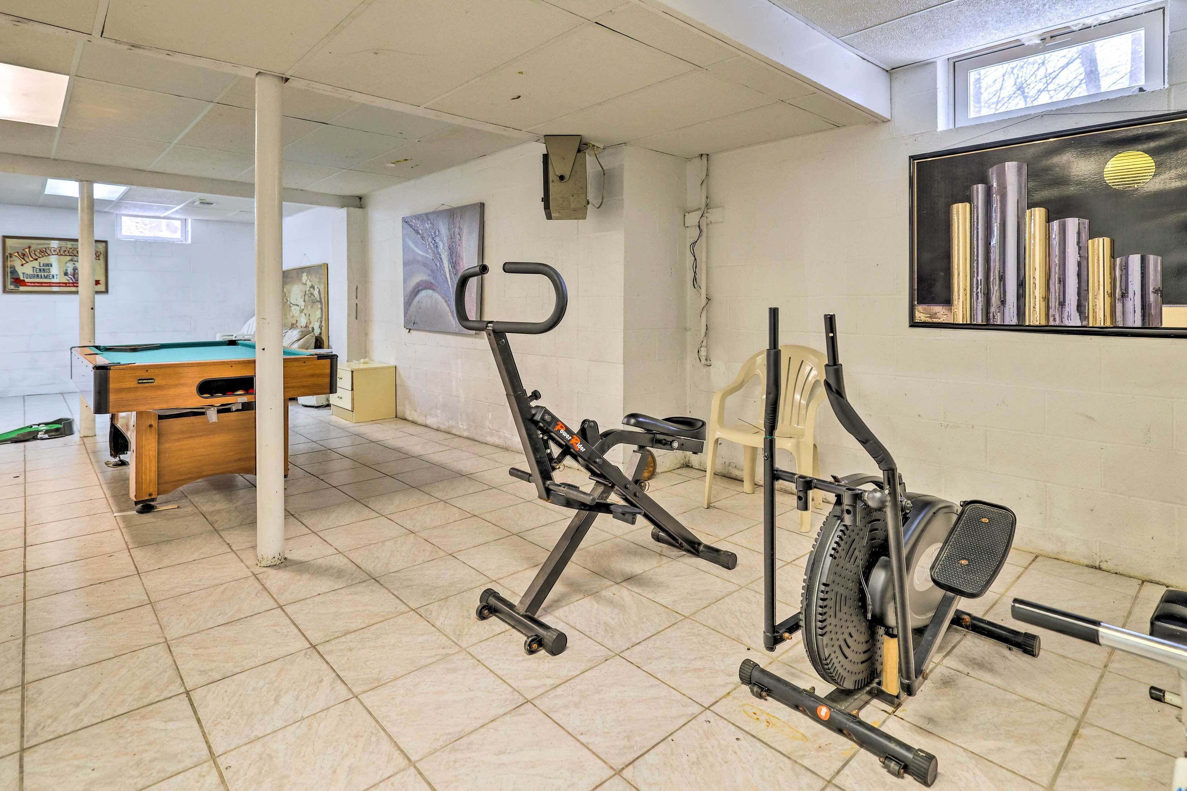 Een kamer met een pooltafel, fitnessapparatuur en een schilderij aan de muur.