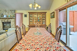 A dining room with a long table, chairs, a fireplace, and a large wooden cabinet.
