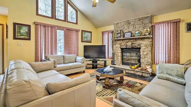 A living room with a stone fireplace, a flat-screen TV, and a large window.
