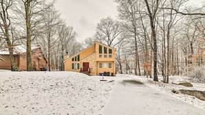A two-story house with a red door and a small front yard, surrounded by leafless trees and a snow-covered ground.