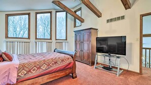 A bedroom with a bed, a television on a stand, a cabinet, and large windows.