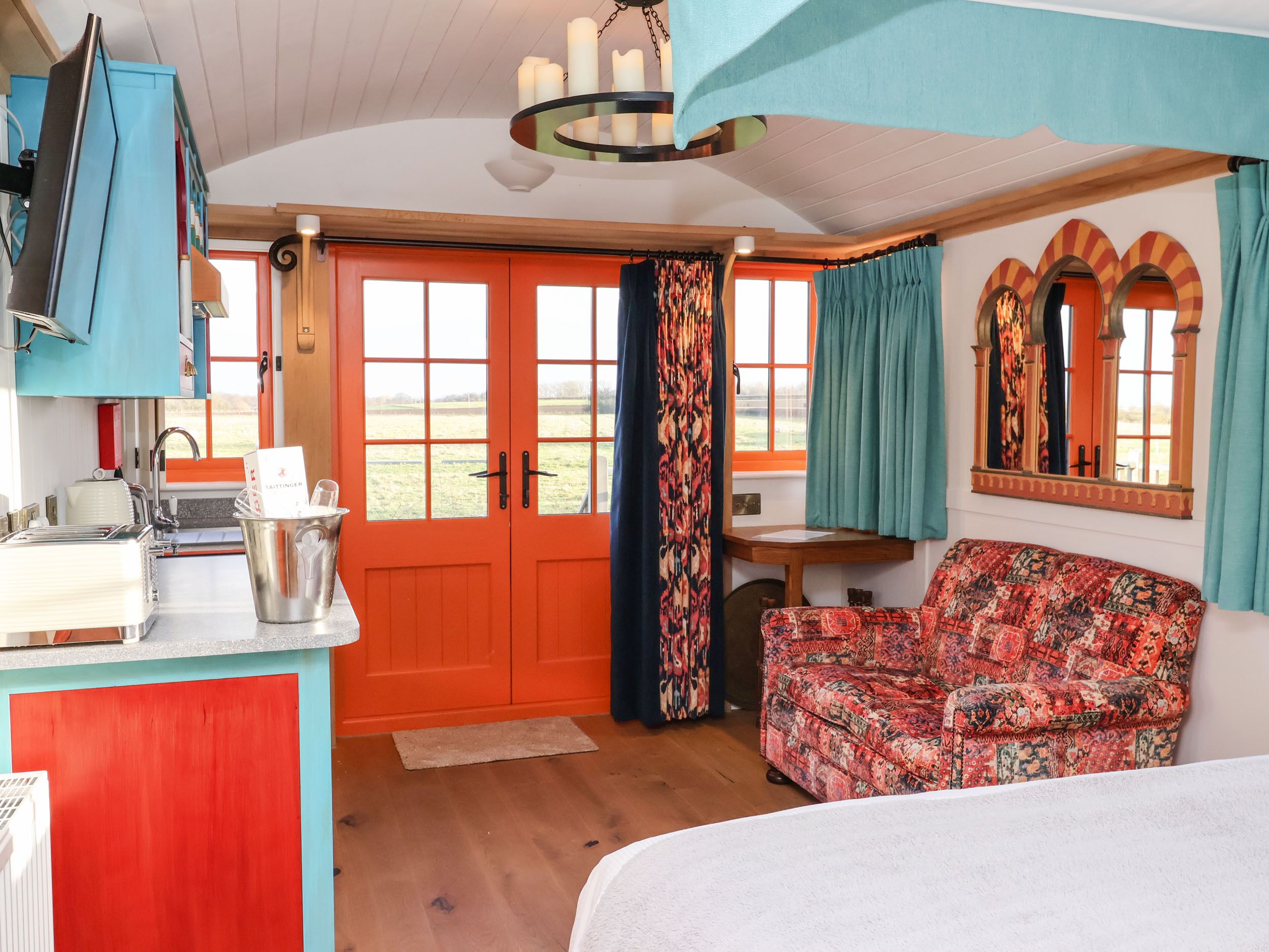 A cozy room with a wooden ceiling, a red door, a patterned sofa, a small table, and a television.