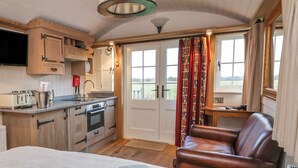 A cozy room with a bed, a leather chair, a kitchenette, and a large window with curtains. - The White Princess (York)