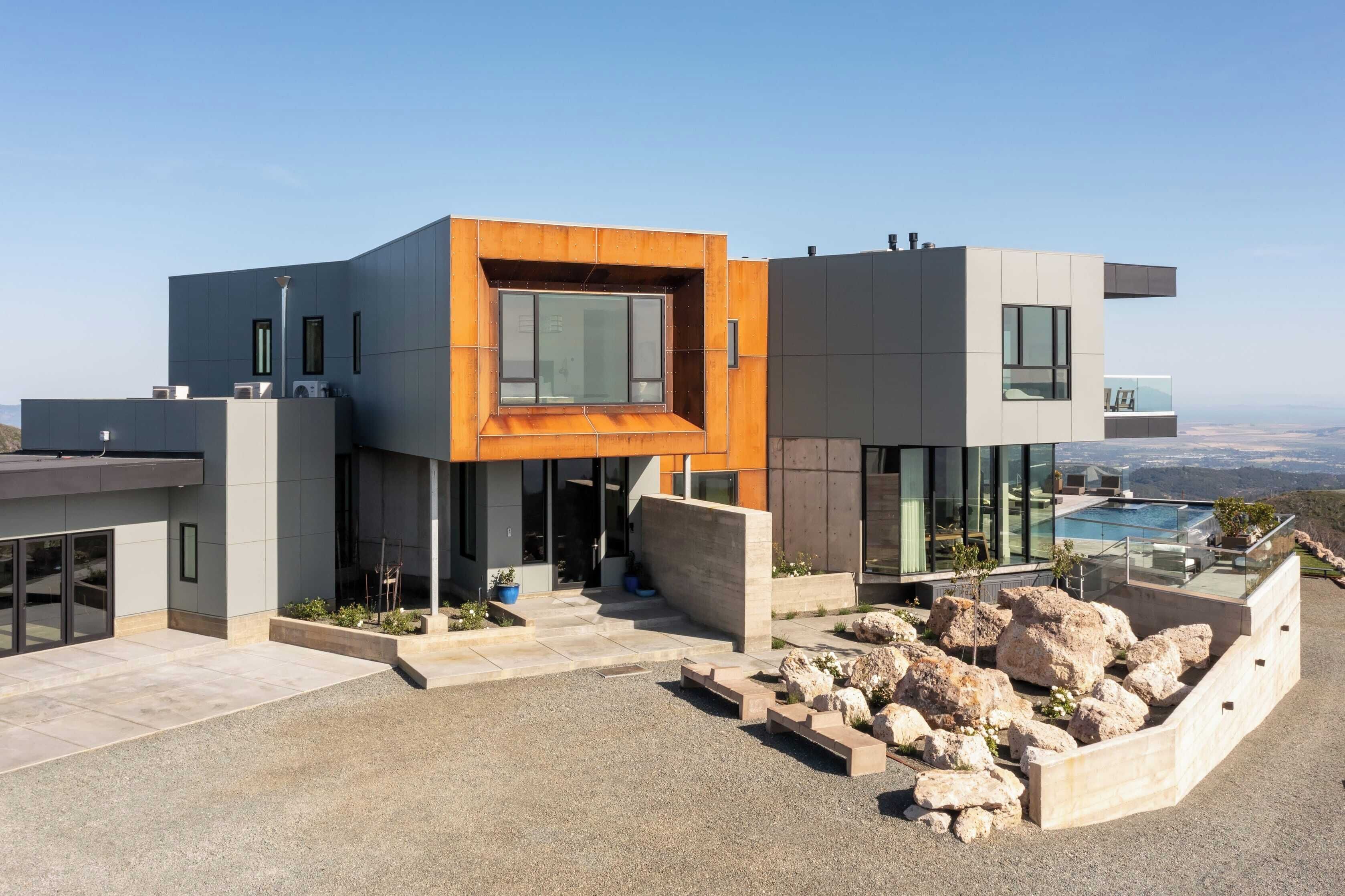 Una casa moderna de varios pisos con una sección anaranjada destacada, ventanas amplias y un área de piscina.