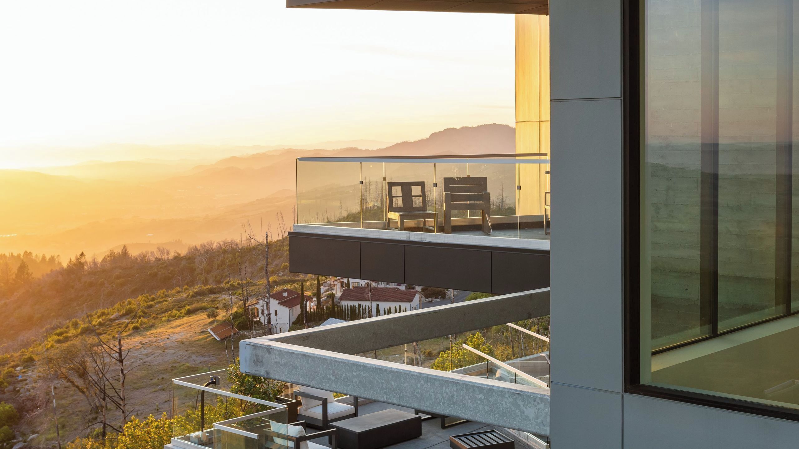 Un edificio moderno con un balcón de vidrio que da a un paisaje montañoso.