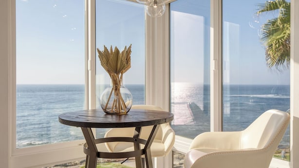 A round table with a clear glass vase and a chair by a large window overlooking the ocean. - Oceanfront in La Jolla, Steps to Beach, Shops, Dining Dawn Patrol by Avantstay (La Jolla)