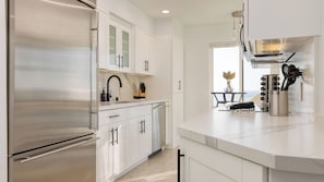 A modern kitchen with stainless steel appliances, white cabinetry, and a view to the outside. - Oceanfront in La Jolla, Steps to Beach, Shops, Dining Dawn Patrol by Avantstay (La Jolla)