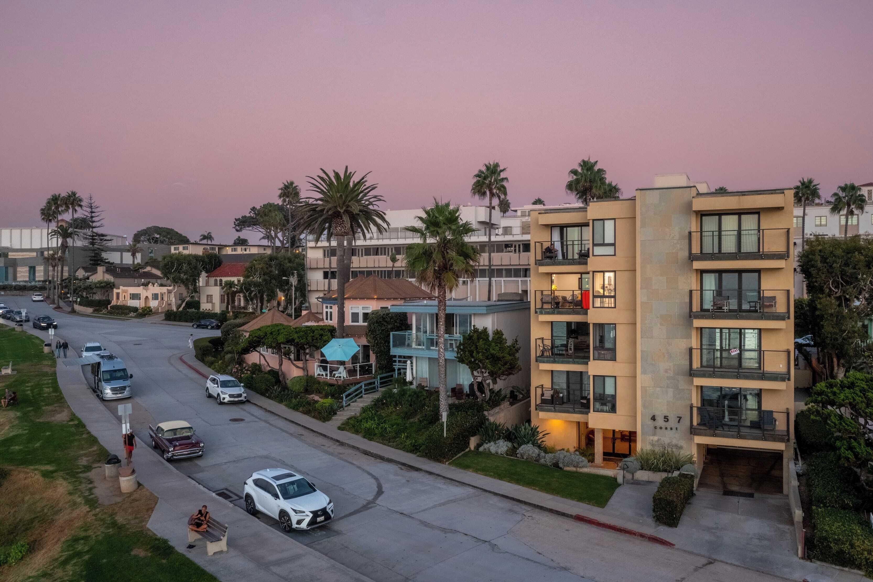 Un immeuble moderne à plusieurs étages, doté de balcons, d’une allée et de voitures garées.