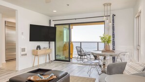 A modern living room with a flat-screen TV, a wooden side table, a glass dining table with chairs, a leather sofa, and a balcony with a view of the sea. - Oceanfront in La Jolla, Steps to Beach, Shops, Dining Dawn Patrol by Avantstay (La Jolla)
