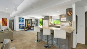 A modern kitchen with a central island, bar stools, and a dining area with a sofa and chairs. - Modern Oasis w/ Pool, Patio Lounge, & Mountain Views Palo Verde by Avantstay (Palm Springs)