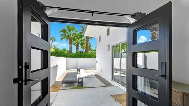 A modern open-plan living area with a large sliding glass door leading to a patio with a concrete floor and a small seating area. - Modern Oasis w/ Pool, Patio Lounge, & Mountain Views Palo Verde by Avantstay (Palm Springs)