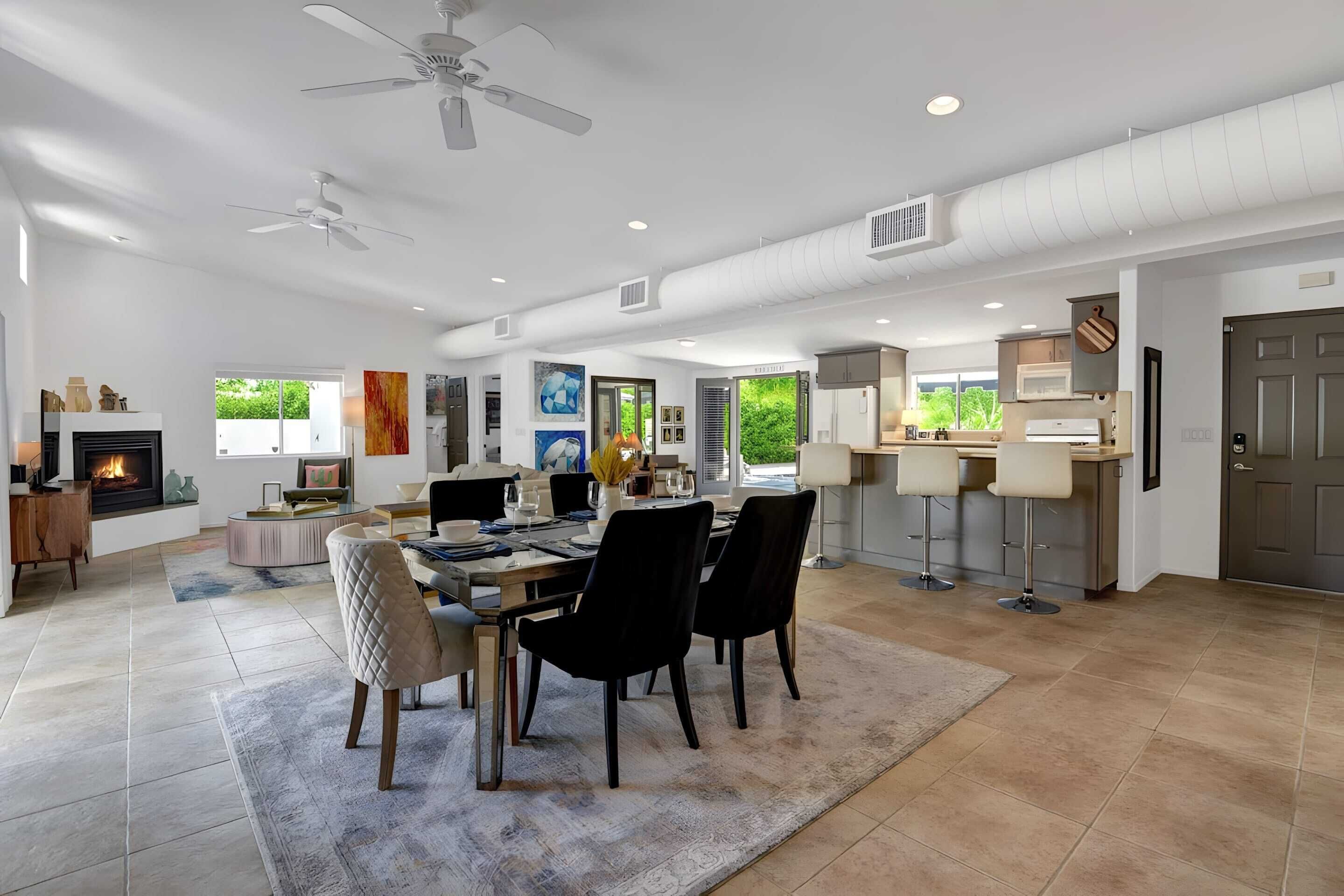 A spacious living area with a fireplace, dining table, and chairs. There is a kitchen area with bar stools and a large window.