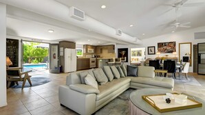 A modern living room with a sectional sofa, a glass coffee table, and a dining area with a kitchen in the background. - Modern Oasis w/ Pool, Patio Lounge, & Mountain Views Palo Verde by Avantstay (Palm Springs)