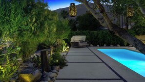 Un espace aménagé au bord de la piscine, comprenant un chemin, un espace salon couvert et des lanternes décoratives.