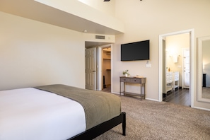 A bedroom with a bed, a bedside table, a TV mounted on the wall, and a walk-in closet.
