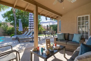 An outdoor patio with lounge chairs, a pool, and a dining area with a table set for a meal.