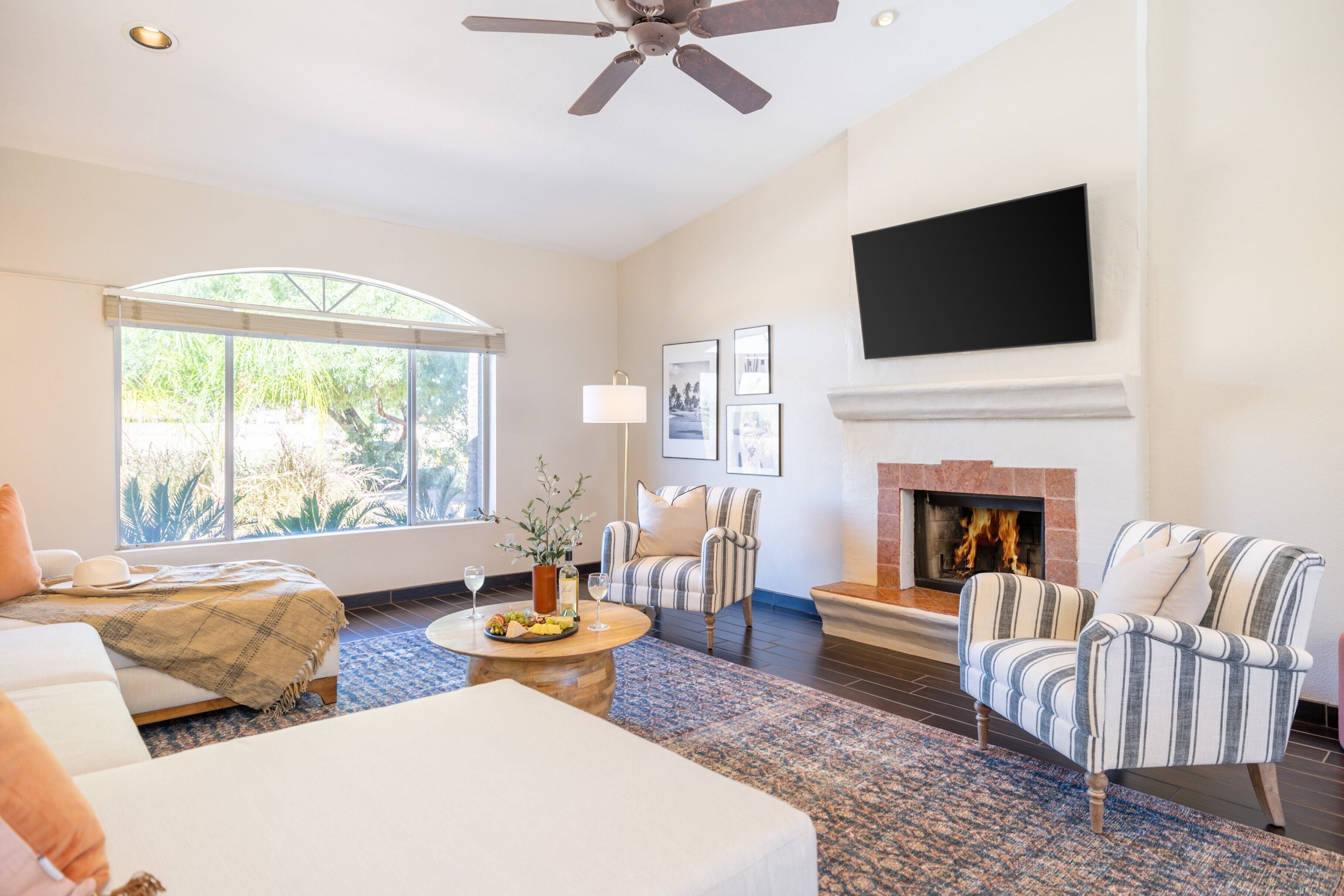 A spacious living room with a fireplace, a large TV mounted on the wall, and a comfortable seating area with striped armchairs and a sofa.